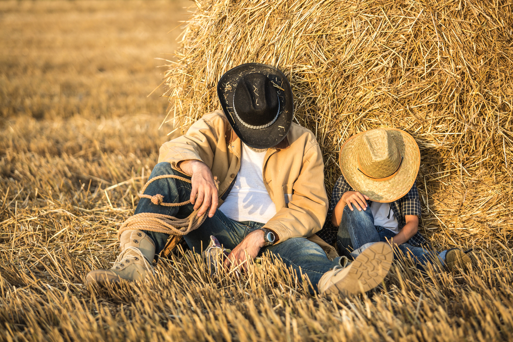 Photo of a farmer and a son in front of a round bale
